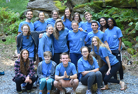 A group of students in matching shirts posing as a group in a forest