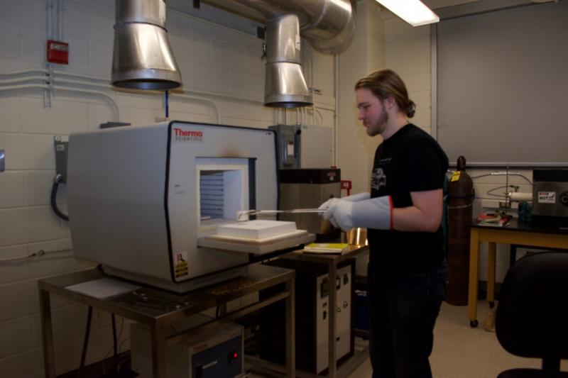 A student uses tongs and gloves to place an item in a furnace