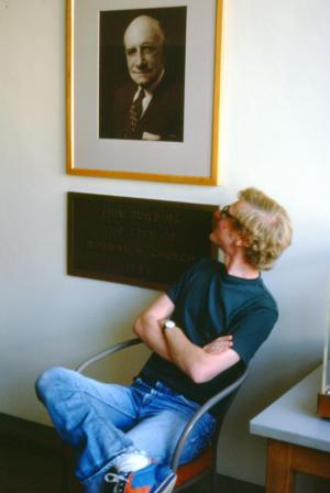 Beratan sitting in a chair and looking up at a portrait on the wall