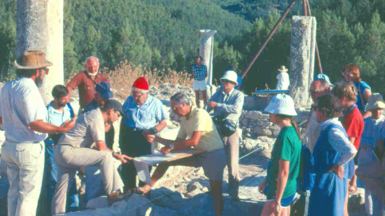 A large group gather around a sig site as a man is shown a find