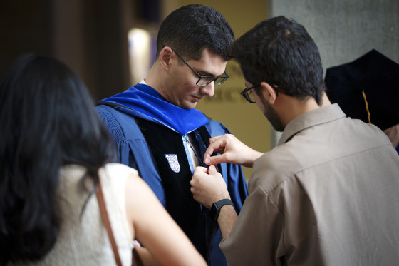 graduate gets help with his cap and gown at Math graduation ceremony