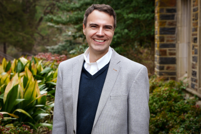 A man wearing a gray jacket and smiling